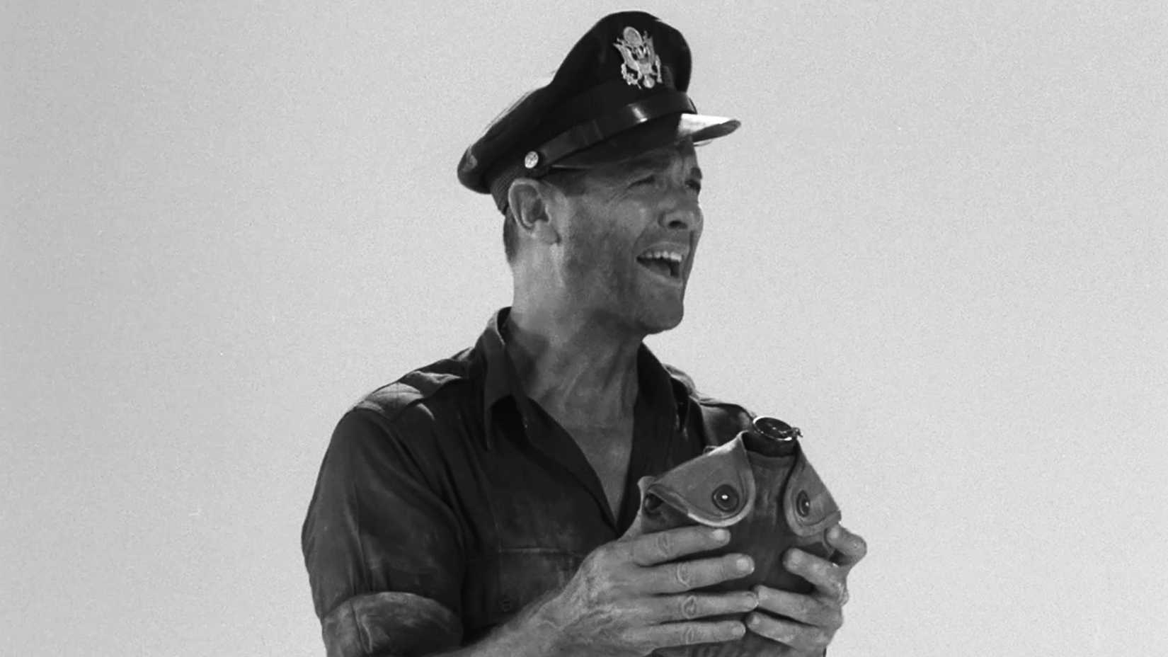 A military officer in a service cap holds a canteen in the desert in The Twilight Zone episode “King Nine Will Not Return.”