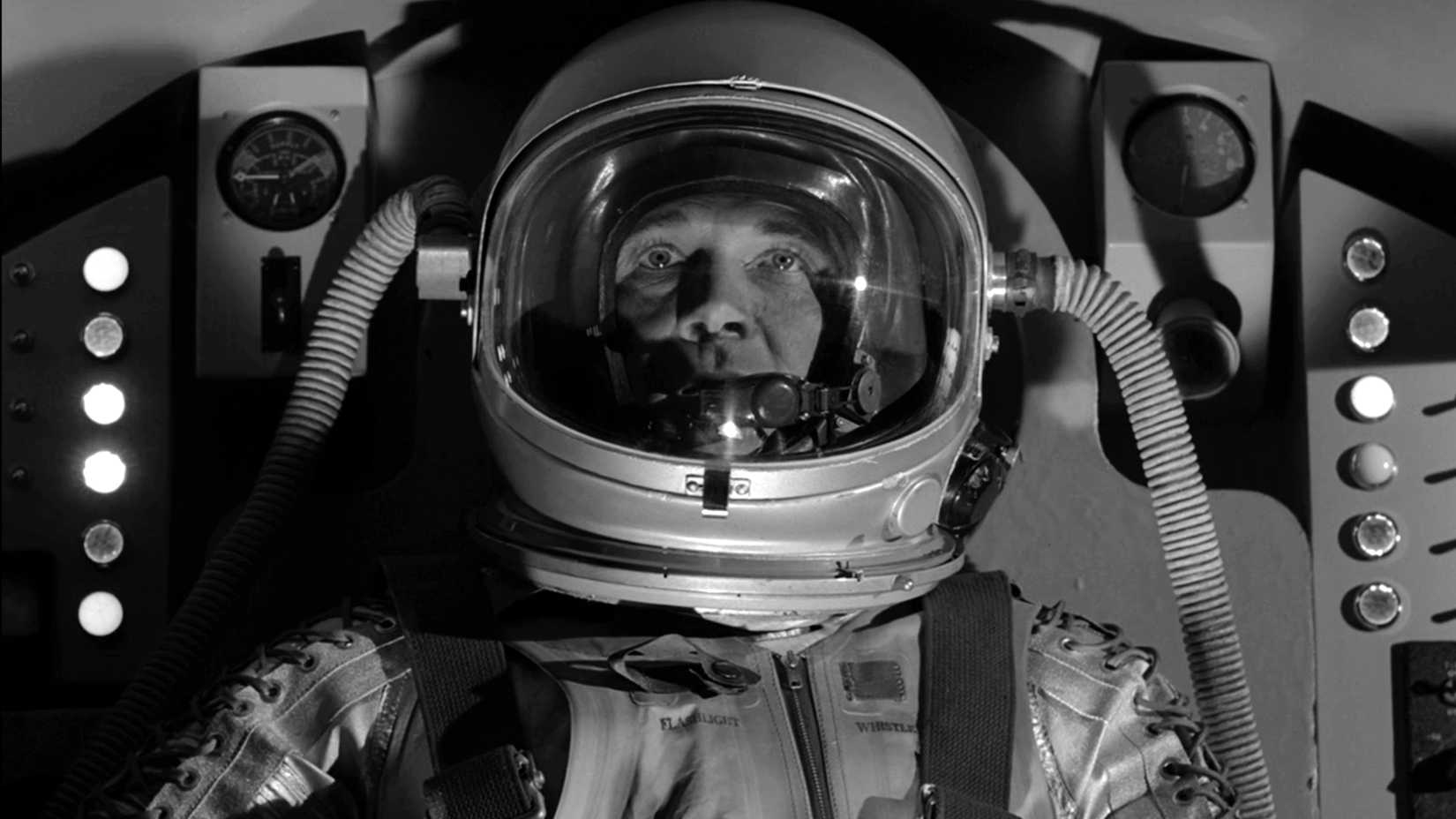 An astronaut wearing a pressure suit and helmet sits inside a spacecraft in The Twilight Zone episode “The Parallel.”