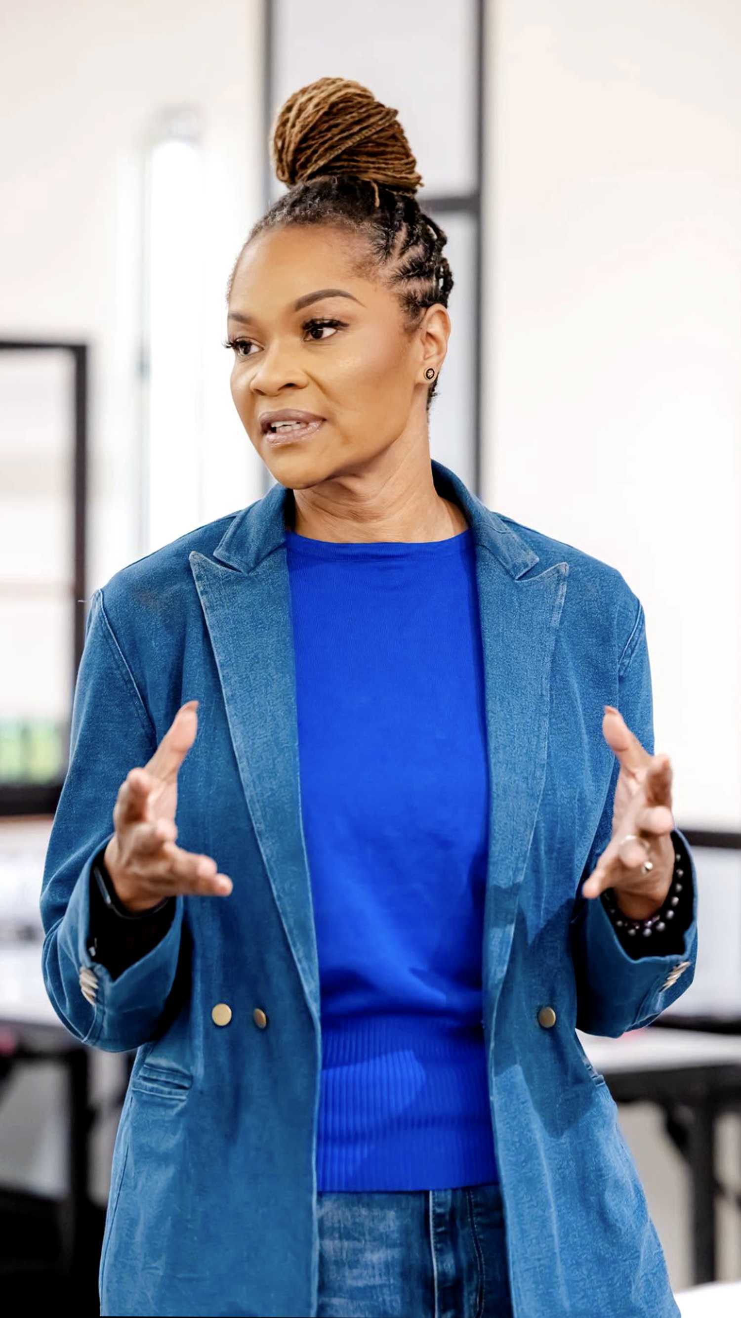 Jas Boothe gestures with both hands while wearing a blue shirt and denim blazer.